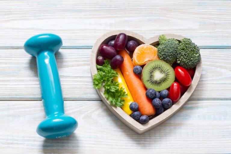 Dumbbell and heart-shaped bowl of fruits and veggies, suggesting heart health.