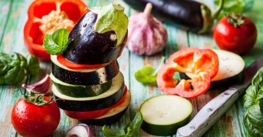 Slices of raw zucchini, eggplant, and red peppers in a stack