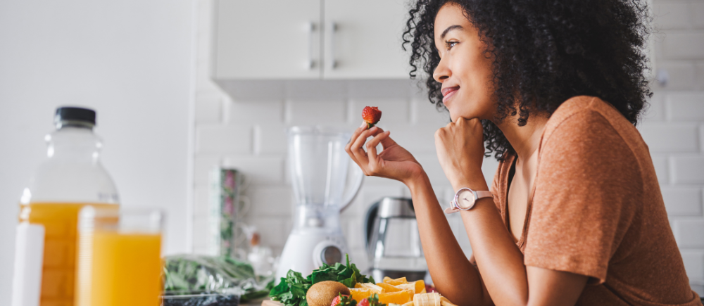 Woman looking forward and smiling while eating a strawberry and others healthy plant foods in her kitchen