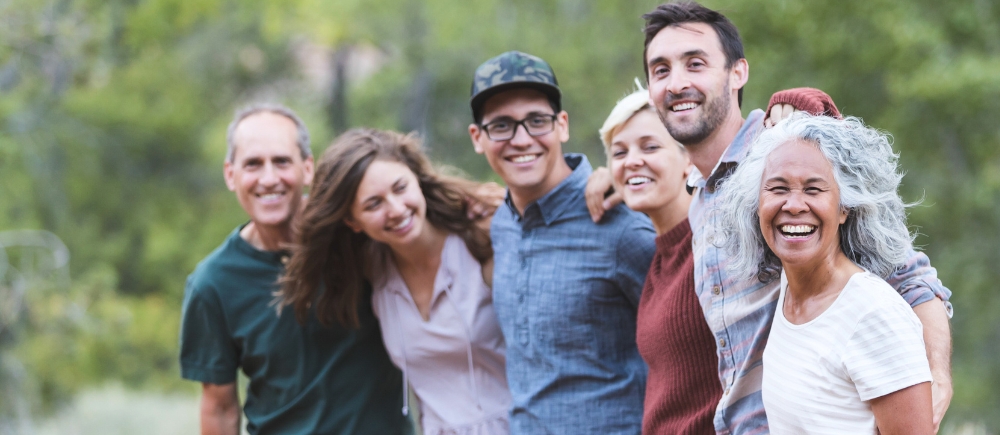A group of friends with their arms over one another smiling out in nature.