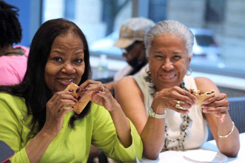 Two ladies smiling and eating a plant-based, whole-grain, pita sandwich