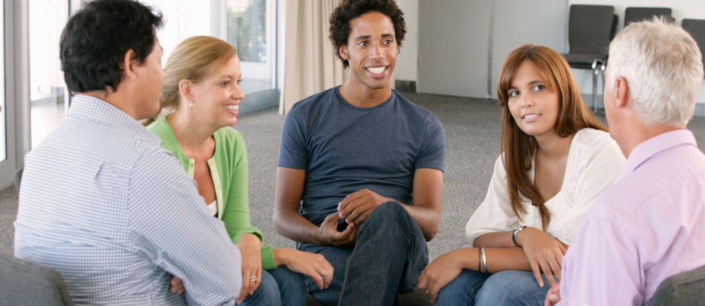 Group of adults smiling and sitting in a circle and listening to one another.