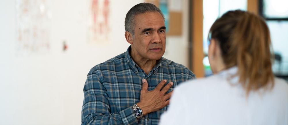 Man with his hand over his chest looking intently at a female medical professional, as she looks back at him.