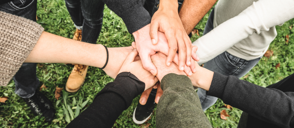 A diverse group of people, standing in a circle, with their hands stacked together in the center.